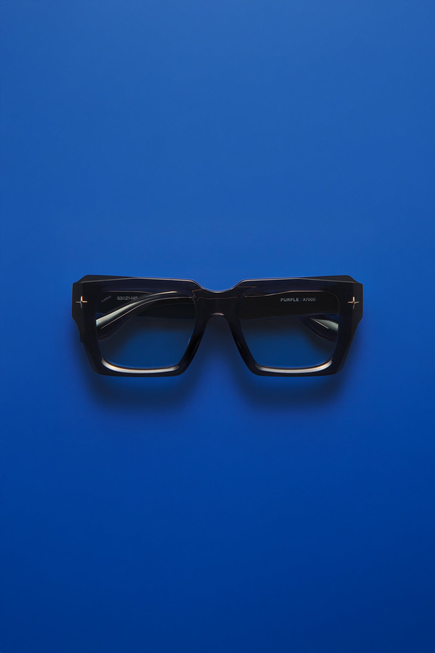 Black square eyeglass frames with dark lenses, photographed flat against a solid blue background.