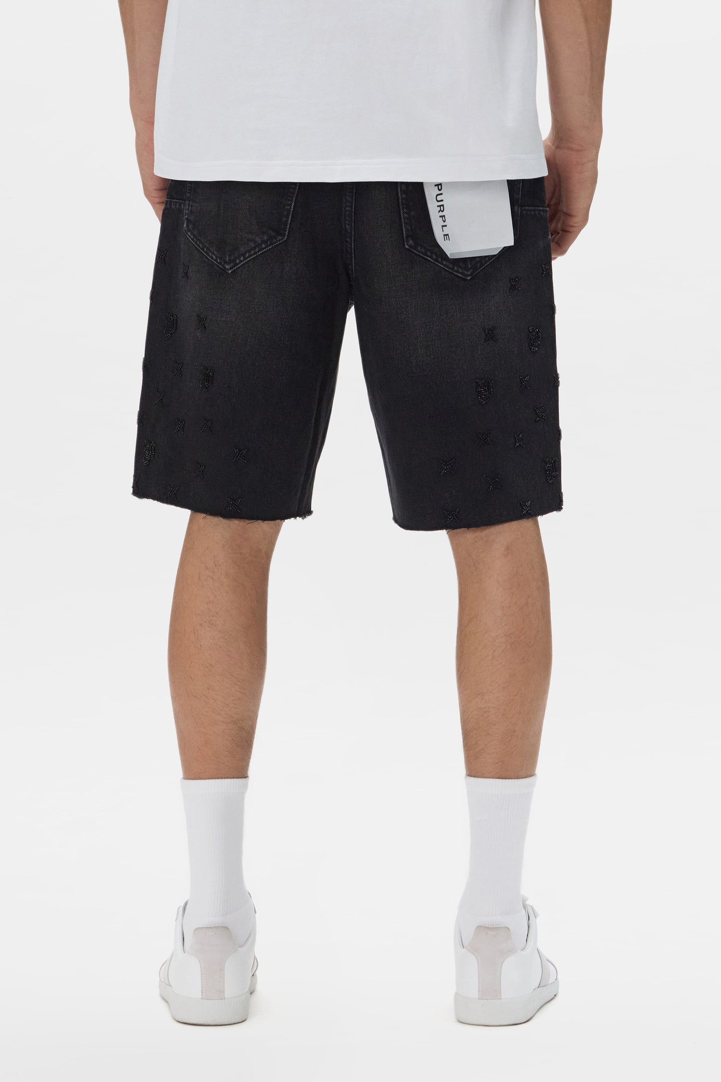 Person wearing black distressed denim shorts on a white background