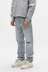A person wears the PURPLE BRAND P011 Jacquard Monogram light grey sweatshirt, mid-rise ripped knee straight leg jeans, and white sneakers, standing against a plain white background.