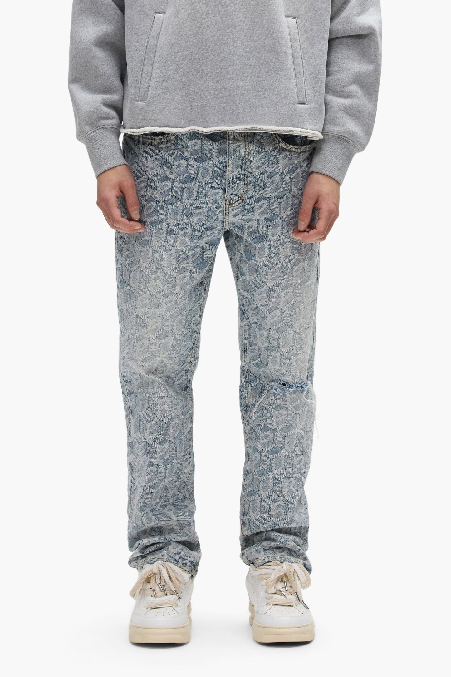 A person wears a gray sweatshirt, white sneakers, and PURPLE BRAND P011 Jacquard Monogram light blue mid-rise straight leg jeans. They stand facing forward with hands at their sides; only their body from shoulders to feet is visible.